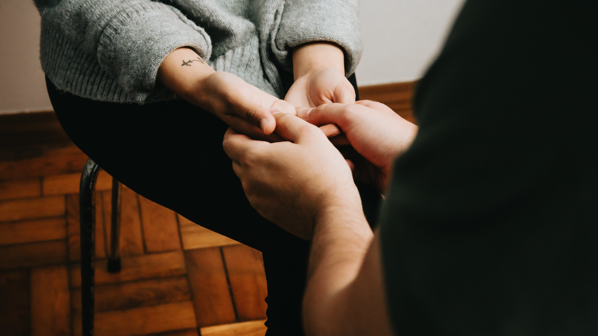 Person receiving a hand massage in a setting with wooden flooring.